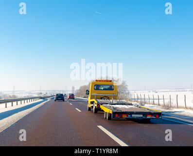 Yellow tow truck with empty platform moves on the highway in winter Stock Photo