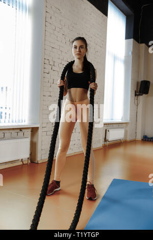 Woman with battle ropes exercise in the fitness gym. Athlete, sport, rope, training, workout, exercises and healthy lifestyle concept Stock Photo