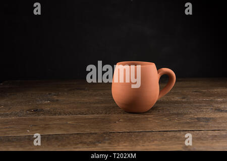 Empty unpainted clay pot on wooden table with black background Stock Photo