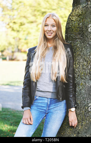 young woman leaning against tree in park Stock Photo