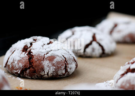 Chocolate cookies with cracks on baking paper and iolated on black. Cracked chocolate biscuits. Stock Photo