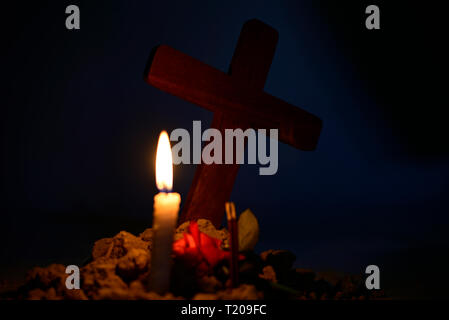 Giving respect to human soul. Give a candle and rose under Jesus cross in cemetery on moonlight. Stock Photo