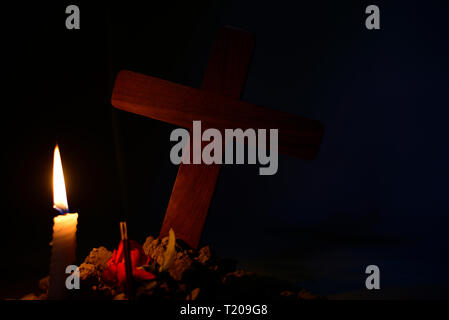 Giving respect to human soul. Give a candle and rose under Jesus cross in cemetery on moonlight. Stock Photo