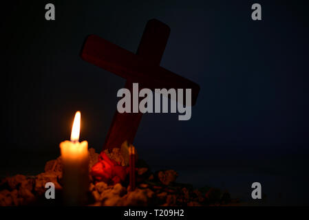 Giving respect to human soul. Give a candle and rose under Jesus cross in cemetery on moonlight. Stock Photo