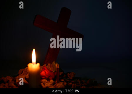 Giving respect to human soul. Give a candle and rose under Jesus cross in cemetery on moonlight. Stock Photo