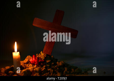 Giving respect to human soul. Give a candle and rose under Jesus cross in cemetery on moonlight. Stock Photo