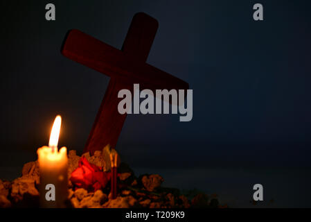 Giving respect to human soul. Give a candle and rose under Jesus cross in cemetery on moonlight. Stock Photo