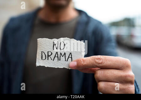 closeup of a young caucasian man on the street, wearing casual clothes, showing a piece of paper with the text no drama written in it Stock Photo