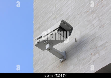 CCTV survaillance camera mounted on white building with blue sky in background Stock Photo