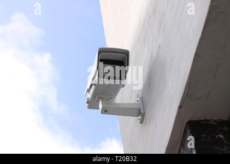 CCTV survaillance camera mounted on white building with blue sky in background Stock Photo