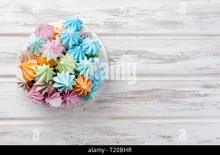colored french meringues on a plate on white wooden background. Copy space. Stock Photo