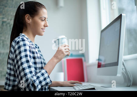 Woman Working At Computer Drinking From Reusable Takeaway Cup Stock Photo