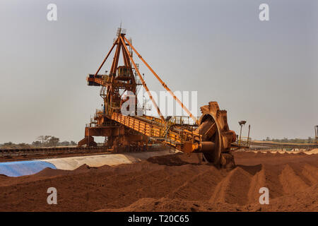 Port operations for managing and transporting iron ore.  Bucket  reclaimmer stacker using bucket wheel to move lump ore to conveyor before shipping. Stock Photo