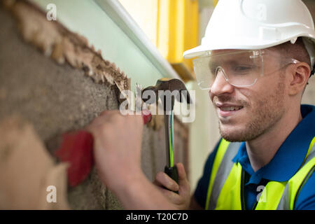 Construction Worker With Chisel Removing Plaster From Wall In Renovated House Stock Photo