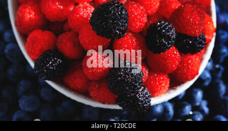 Assortment of fresh red and black berries. Top view of raspberries in the plate on background of blueberries. Ripe and juicy fresh raspberries close-u Stock Photo