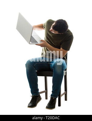 Perplexed young man freelancer or programmer sitting on chair lifting his laptop looking to fix some problems, full length portrait isolated over whit Stock Photo