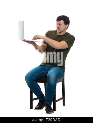 Scared young man freelancer or programmer sitting on chair holding his laptop pressing a button on keyboard, full length portrait isolated over white  Stock Photo