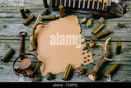 Paper for information on old wooden background and deer horn, trap and cartridges beside. Hunting equipment on vintage board. Top view Stock Photo