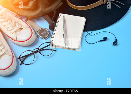 Flat lay travel accessories on blue background with hat, backpack, eyeglasses, clock, pen, shoes and notepad. Top view, copy space. Travel or vacation Stock Photo