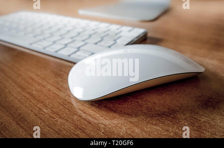 White wireless mouse on office desk with keyboard behind. Stock Photo