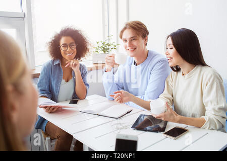 Nice picture of four students having fun together. They are sitting at the table and studying Stock Photo