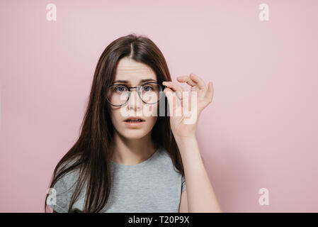 Portrait of shocked pretty young female stares through eyewear, cant believe her eyes, being emotional, being in stupor from sudden news, dressed in t Stock Photo