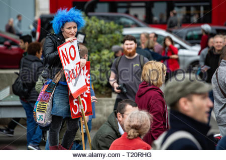 A woman in a blue wig and holding a No Brexit sign looks ruefully at a crown at Marble Arch Stock Photo