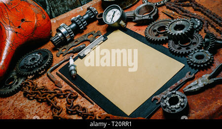 Clipboard with vintage paper in the center of rusty tools, gears on old metal background. Motorcycle tools, equipment and repair. Stock Photo