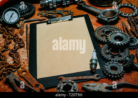 Clipboard with paper in the center of rusty tools, gears on old metal background. Motorcycle tools, equipment and repair. Stock Photo