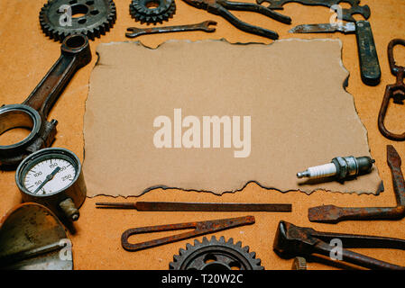 Vintage paper for your info in the center of rusty tools, gears on vintage fiberboard background. Motorcycle equipment and repair template. Stock Photo