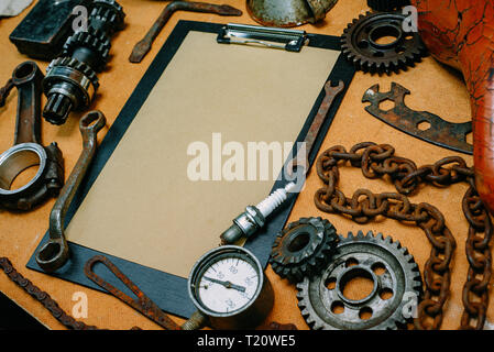 Closeup clipboard with paper for your info in the center of rusty tools, gears on vintage metal background. Motorcycle equipment and repair template. Stock Photo