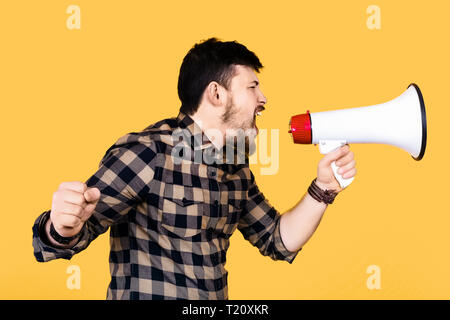 bearded man in shirt shouts into megaphone, image on yellow background, concept of appeal Stock Photo