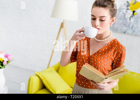attractive elegant young woman in pearl necklace holding book and drinking coffee Stock Photo
