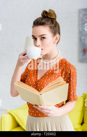elegant young woman in pearl necklace holding book and drinking coffee Stock Photo