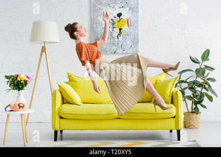 side view of elegant young woman levitating in air in living room Stock Photo