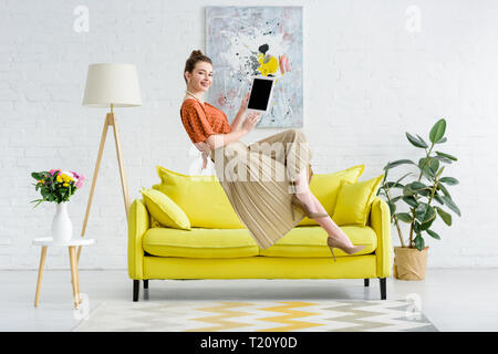 elegant happy young woman levitating in air and showing digital tablet with blank screen in living room Stock Photo