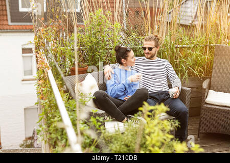 Young couple relaxing on their balcony, sitting on couch Stock Photo