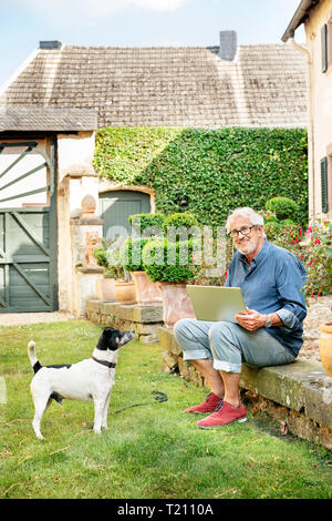 Portrait of smiling senior man with dog in garden using tablet Stock Photo