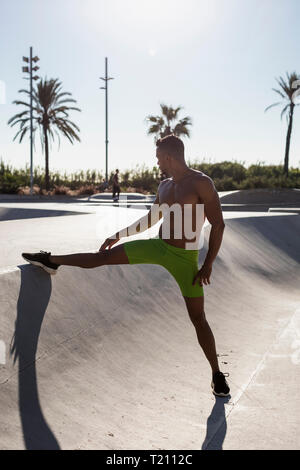 Barechested muscular man doing stretching exercise in a skatepark Stock Photo