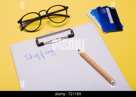 List of paper with words shopping list, credit cards, pen on yellow background. Copy space. Free space. Stock Photo