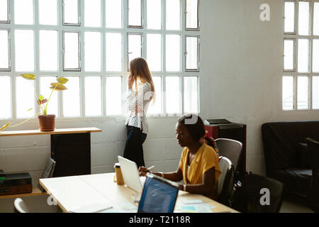 Two women using cell phone and laptop in office Stock Photo