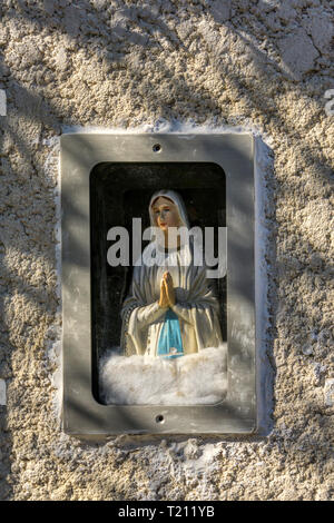 Small religious statue of the Virgin Mary in a niche on the outside of a house in a French village.