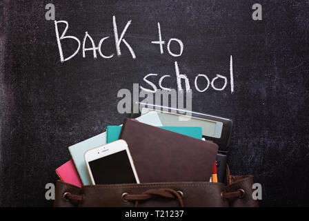 Backpack with school stationery and cell phone on slate background. Back to school text. Top view. School concept. Stock Photo