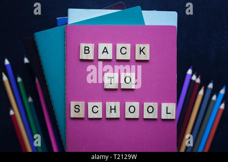 Close-up pile of books, school stationery, wooden words back to school on slate black background. Back to school concept. Top view. Education. Stock Photo