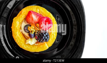 Mini cake decorated with fresh strawberry, raspberry, blackberry, golden dust, and summer berries close-up on a black plate. Beautiful pastry, small c Stock Photo