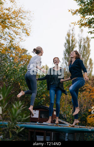 Happy mother with two teenage girls jumping on trampoline in garden in autumn Stock Photo