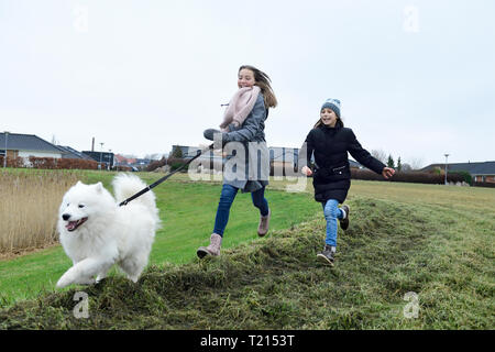 Two girls running on a meadow with dog having fun Stock Photo
