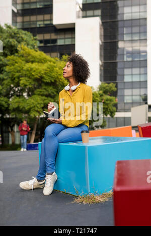 Woman sitting on bench with smartphone and coffee writing in notebook Stock Photo