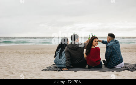 Woman sitting with friends toasting beers at the beach. Four friends partying on the beach. Stock Photo
