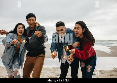 Group of asian friends having fun with sparklers at the beach. Group of young men and women celebrating new year's day at the beach. Stock Photo